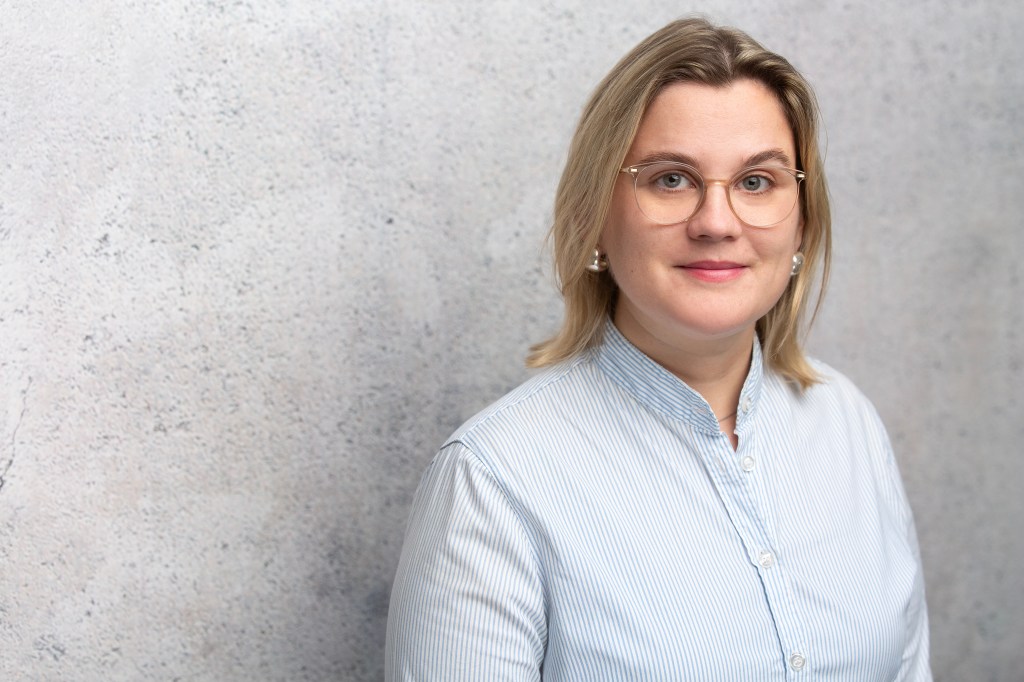 Porträtbild von Laura Müller in einer hellen Bluse vor einer grauen Wand
